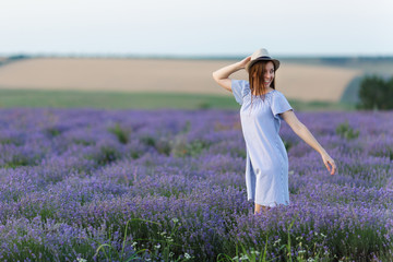 Fototapeta na wymiar Portrait of young smiling beautiful woman in blue dress, hat on purple lavender flower blossom meadow field outdoors on summer nature, Provence. Happy female run at flowering bush. Lifestyle concept.
