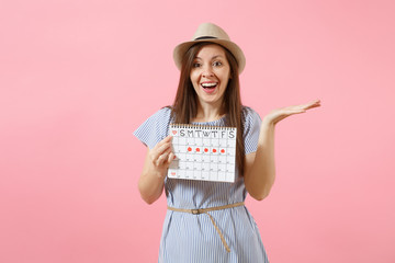 Portrait of excited woman in blue dress, hat holding periods calendar for checking menstruation days isolated on bright trending pink background. Medical, healthcare, gynecological concept. Copy space