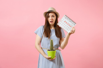 Sad sickness woman in blue dress holding green cactus, periods calendar for checking menstruation days isolated on pink background. Medical, healthcare, gynecological, tummy pain concept. Copy space.