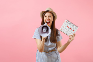 Angry expression wild woman screaming in megaphone, holding periods calendar for checking menstruation days isolated on pink background. Medical healthcare, pms mood, gynecological concept. Copy space