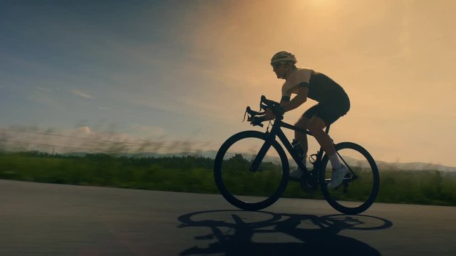 Close up, low angle, wide tracking shot of a single cyclist on countryside road