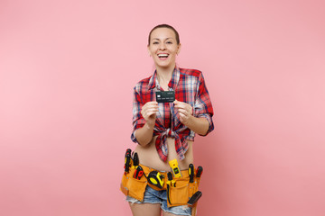 Young smiling handyman woman in plaid shirt, denim shorts, kit tools belt full of variety...