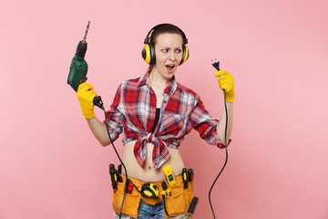Energy sexy handyman woman in gloves, noise insulated headphones, kit tools belt full of...