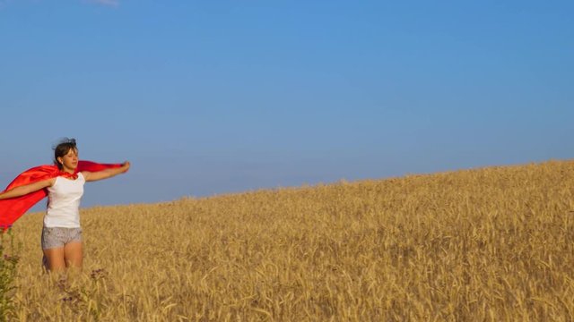 Girl plays superhero running across field with wheat under blue sky.