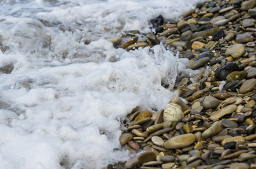pebble stones on the sea beach, the rolling waves of the sea with foam