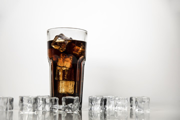 A refreshing drink of stake is poured into a glass beaker. Cola on white background with scattered ice cubes.