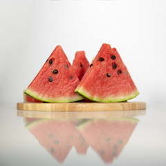 Berry watermelon in water splashes on a wooden tray. Reflection on table.