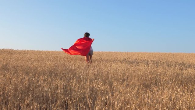 Girl in red raincoat plays superhero in field with wheat.