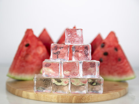 Berry watermelon in water splashes. Cubes of ice in droplets of water are stacked in a pyramid. White background on photo.