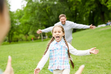 Fototapeta premium Cheerful and funny little girl running to her mother with young man moving behind