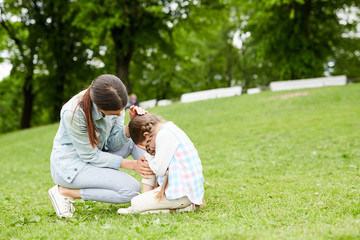 Little girl crying while sitting on green lawn and her mother comforting her