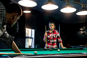 Young couple playing billiard, woman looking after boyfriend