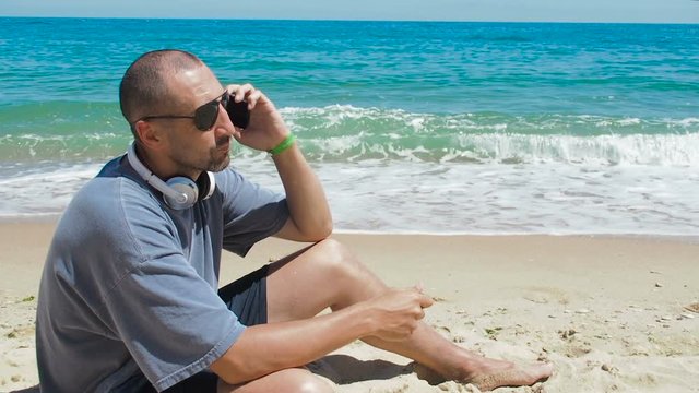 A man on the beach with a phone. A man by the sea is talking on the phone.
