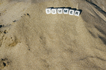 Summer concept made with dice with letters on the wet sand of a beach and marine motives.