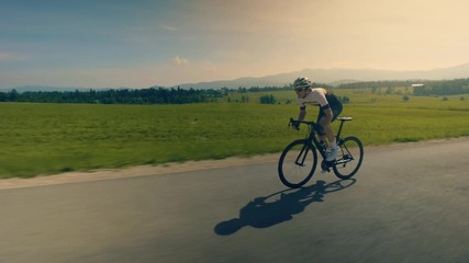 Wide tracking shot of a single man cyclist on the countryside road