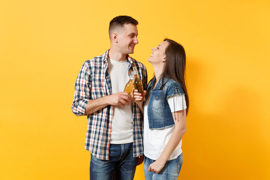 Young smiling couple woman and man sport fans in casual clothes cheer up support team clinking beer bottles looking at each other isolated on yellow background. Sport family leisure lifestyle concept.