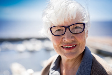 Smiling white haired female in eyeglasses looking at you while enjoying summer vacation