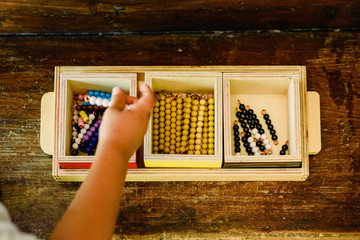 Hands of a child manipulating educational beads  materials to learn to count in a Montessori classroom.