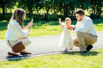 happy and stylish family in the summer in the park. family photosession of beautiful mother, bearded father and cute daughter looking at phone