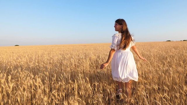 happy girl in white dress runs and smiles on field of ripe wheat, slow motion