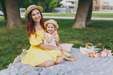 Joyful woman play and sit on green grass in park, rest and hug hold soap bubble blower with little...