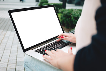 Back view of woman student is work on laptop keyboard on outdoors in urban. Close-up female freelancer is typing text on mobile computer with mock up blank copy space