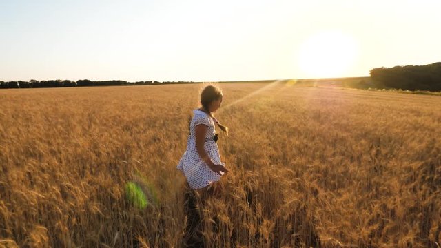 happy little girl playing in field of ripe wheat, on a sunset background, slow motion