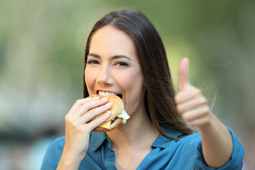 Happy woman eats a burger with thumbs up