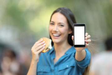 Woman holding a burger showing a phone screen