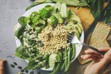 First person view on a dish with raw buckwheat sprouts, broccoli, sticks of asparagus beans,...