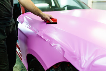 Car wrapping specialist putting vinyl foil or film on car. Selective focus.