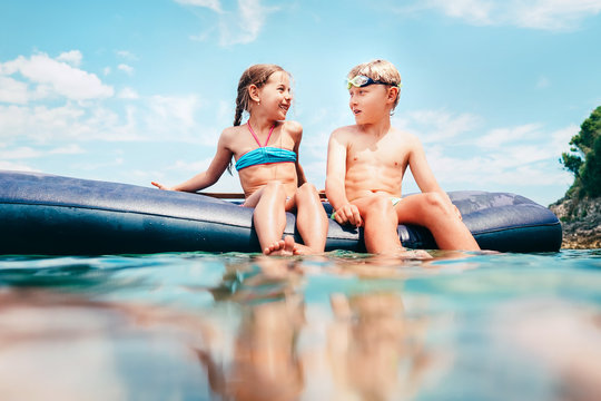 Little sister and brother sit on inflatable mattress in the sea