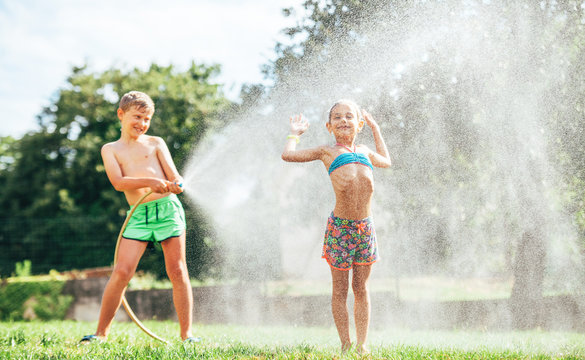 Two happy childs refresh with sprinkling water in hot summer afternoon