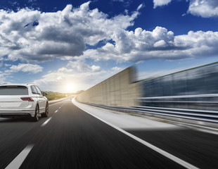 A white car rushing along a high-speed highway in the sun.