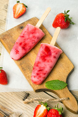 Świeże domowej roboty lody truskawkowe na patyku na drewnianym tle.  © czarny_bez