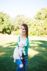 Portrait of beautiful smiling invalid young woman born without upper extremities enjoying with her little white puppy in park.