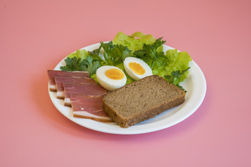 breakfast. Boiled eggs, bacon, greens in a white plate on pink background