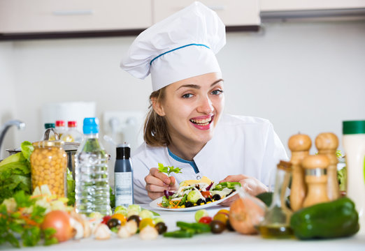 Positive chef decorating salad with parsley in kitchen