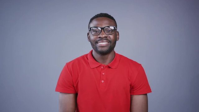 Close up view of attractive Afro-American man putting on nerdy like glasses and charmingly smiling on grey background. Businessman, creative process, brainstorming, office. Male portrait