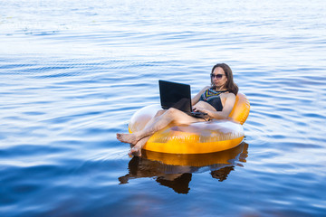 Business woman working on a laptop in an inflatable ring on the sea, the concept of working on...