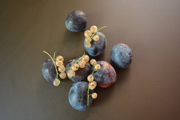 Fresh ripped plums and bunches of white currant on a brown matte background