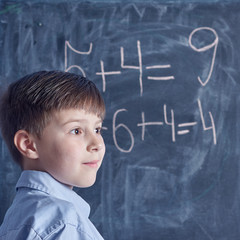 Caucasian schoolboy at a blackboard.  He is thinking over math task.