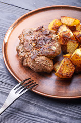 Appetizing piece of fried meat on a large clay plate. Fried potatoes with crispy crust on garnish. Tables are served for lunch and dinner at home, in a restaurant, in the cafe.