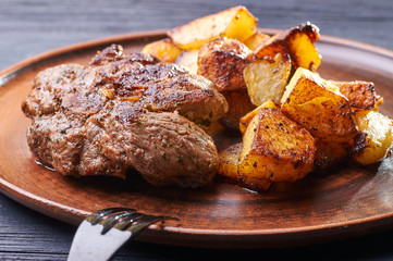 Appetizing piece of fried meat on a large clay plate. Fried potatoes with crispy crust on garnish. Tables are served for lunch and dinner at home, in a restaurant, in the cafe.