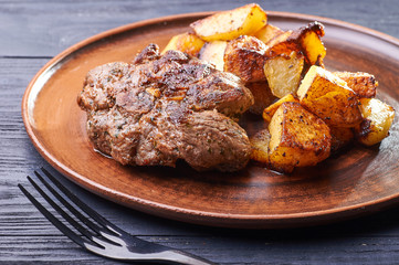 Appetizing piece of fried meat on a large clay plate. Fried potatoes with crispy crust on garnish. Tables are served for lunch and dinner at home, in a restaurant, in the cafe.