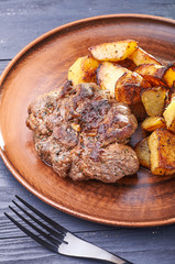 Appetizing piece of fried meat on a large clay plate. Fried potatoes with crispy crust on garnish. Tables are served for lunch and dinner at home, in a restaurant, in the cafe.