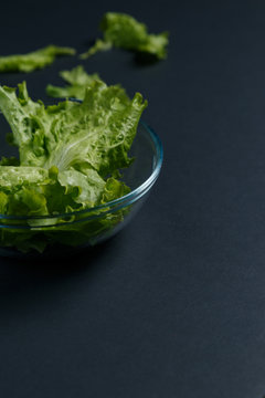 fresh lettuce leaves in glass plate on dark background. Cooking recipe menu restaurant, vertically hi resolution photo with black background and text area or menu design.