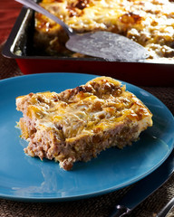 Meat casserole with cheese crust. Appetizing piece of minced meat pie in the foreground. Elegant frying pan with the remains of a pie and a culinary spatula in the background.