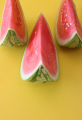 Three slices of fresh watermelon on a colorful, bright yellow background