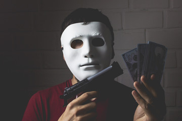 man in a white mask holds a gun in his hand and money